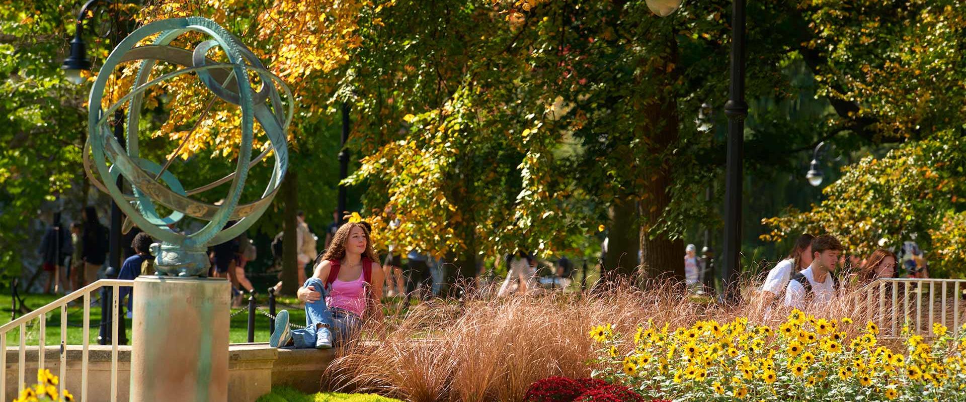 A student enjoys the sunshine while seated beneath the Old Main Armillary Sphere