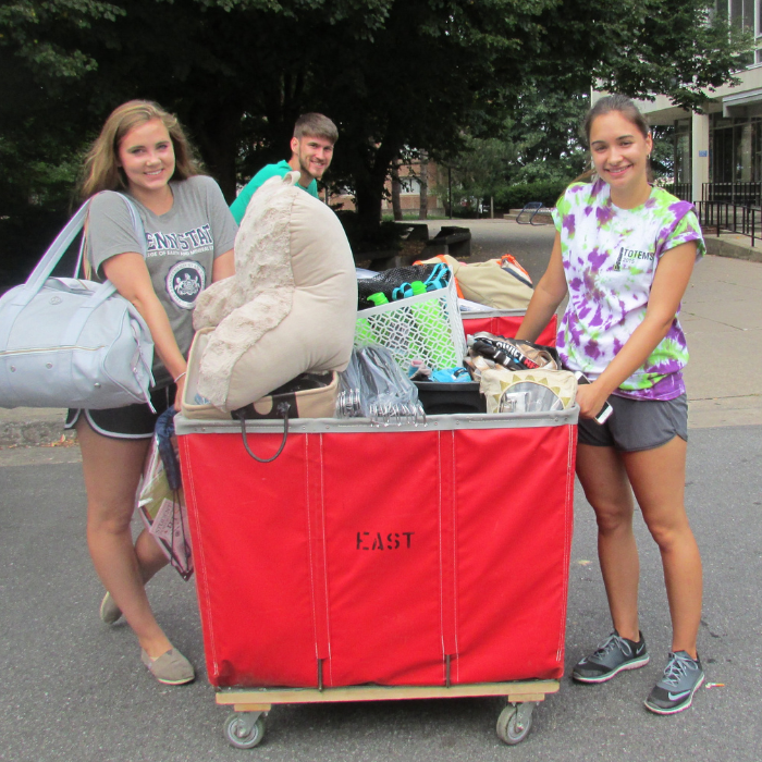 3 students pushing a cart loaded with personal items to move into room