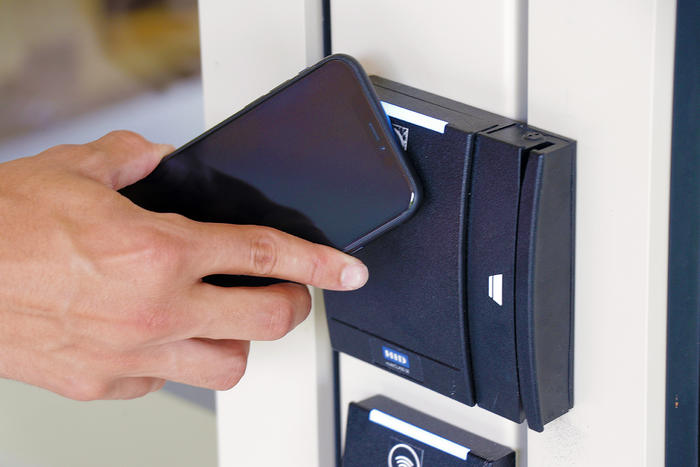 person holding cell phone against a reader device attached to residence hall entry door